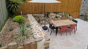 Un patio con una mesa y sillas de madera, un sendero de piedra y una valla de madera.