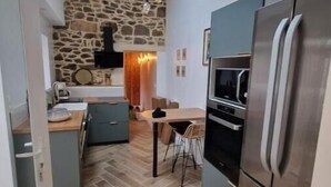 Una cocina compacta con pared de piedra, una mesa de comedor de madera y un refrigerador moderno de acero inoxidable.