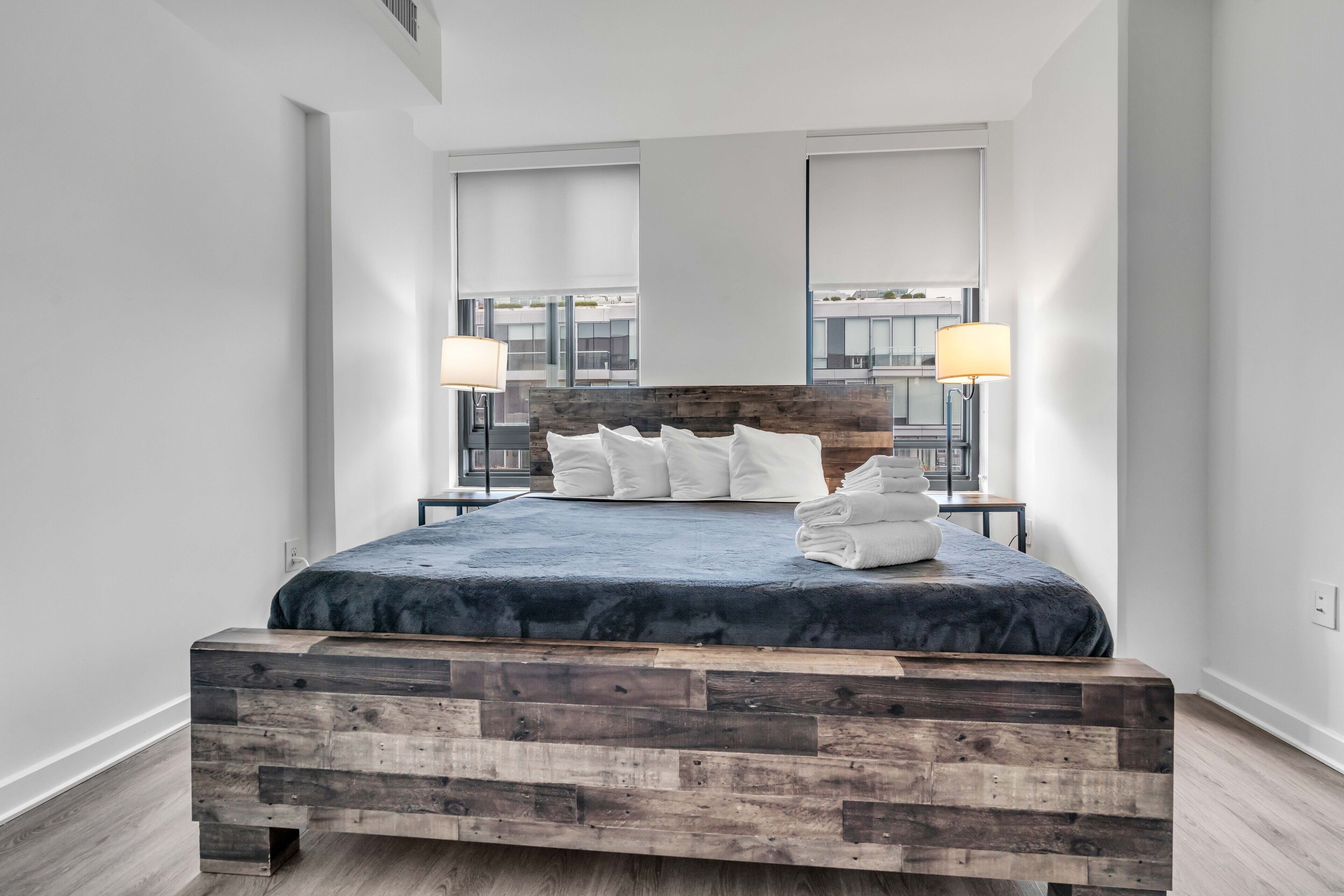 A modern bedroom with a wooden headboard, a large bed with white pillows, and two bedside lamps.