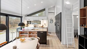 A modern kitchen with a large window, a dining area with a table and chairs, and a built-in bookshelf. - Awesome home in Stege with kitchen (Stege)