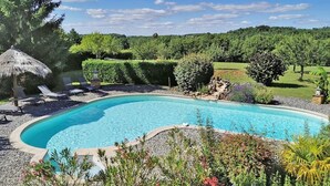 A swimming pool surrounded by a landscaped garden with a thatched-roof structure and lounge chairs. - Charming Gîte in Périgord Noir, Close to the Reference Sites of the Dordogne (Archignac)