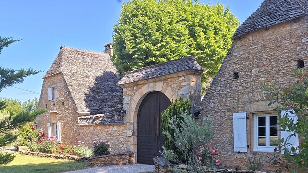 A stone house with a central arched door, surrounded by a well-maintained garden with flowering plants. - Charming Gîte in Périgord Noir, Close to the Reference Sites of the Dordogne (Archignac)