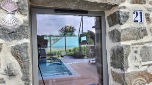 A stone wall with a number plaque '21' and a glass door reflecting a deck area with a pool, outdoor furniture, and a view of the sea. - Krec'h Briand - PLEUBIAN (PLEUBIAN)