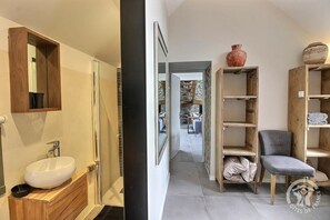 A bathroom with a sink and mirror, a wooden cabinet, and a view into a living area with a staircase and seating.