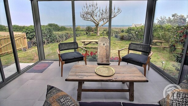 A conservatory with a wooden table and two chairs, a decorative vase, and a view of a garden and distant landscape. - Krec'h Briand - PLEUBIAN (PLEUBIAN)