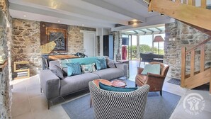 A spacious living area with a stone wall, a grey sofa with blue cushions, a wooden coffee table, and a patterned armchair. - Krec'h Briand - PLEUBIAN (PLEUBIAN)