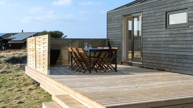 Une terrasse en bois avec une table et des chaises, une porte vitrée et une vue sur les environs.