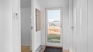 Un couloir avec une porte vitrée donnant sur un espace extérieur, un thermostat fixé au mur et une petite étagère avec une grille métallique.