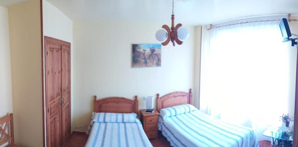 A bedroom with two beds, a wooden wardrobe, a painting on the wall, and a window with curtains.