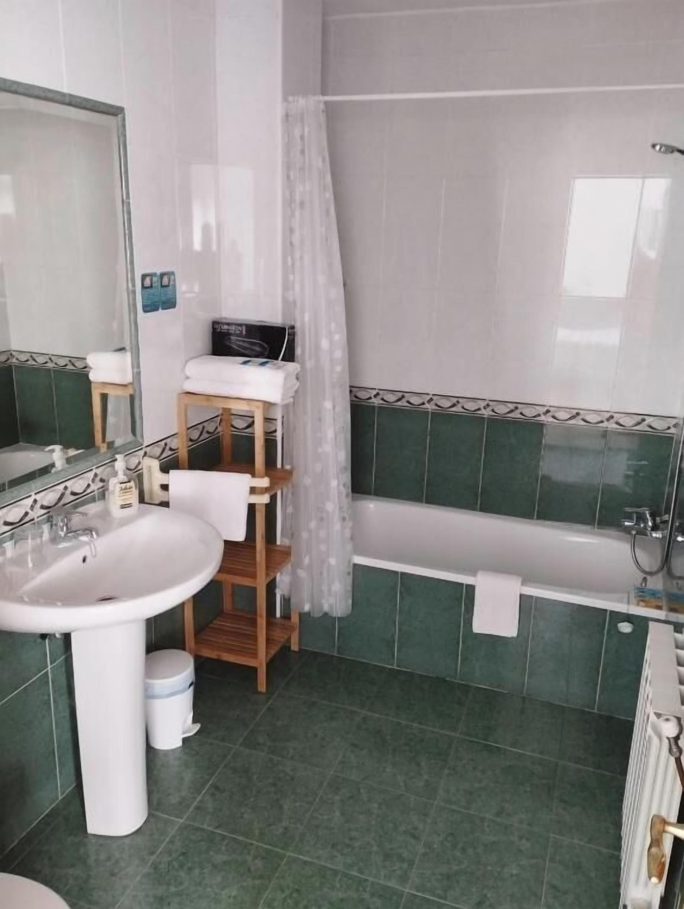Een badkamer met een witte wastafel, een houten plank, een bad en een douchegordijn.