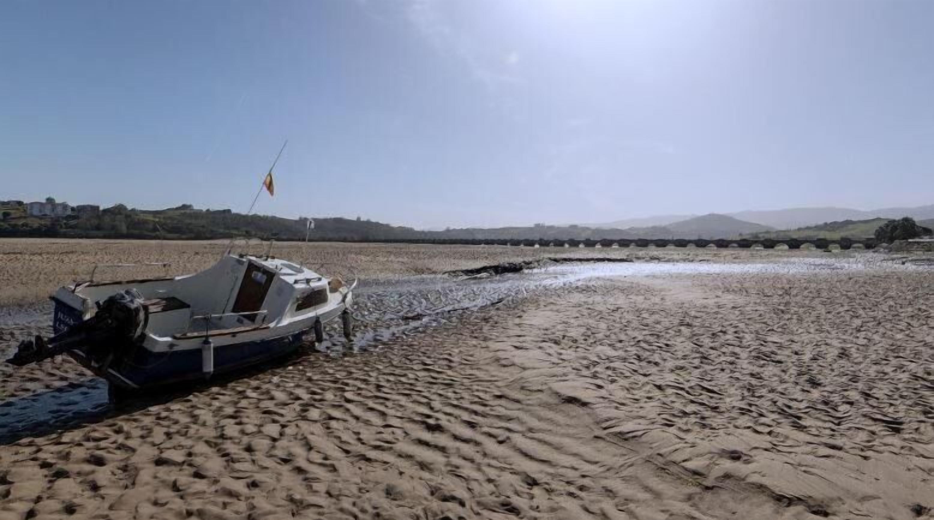 A boat stranded on a sandy beach with a clear sky and distant hills.