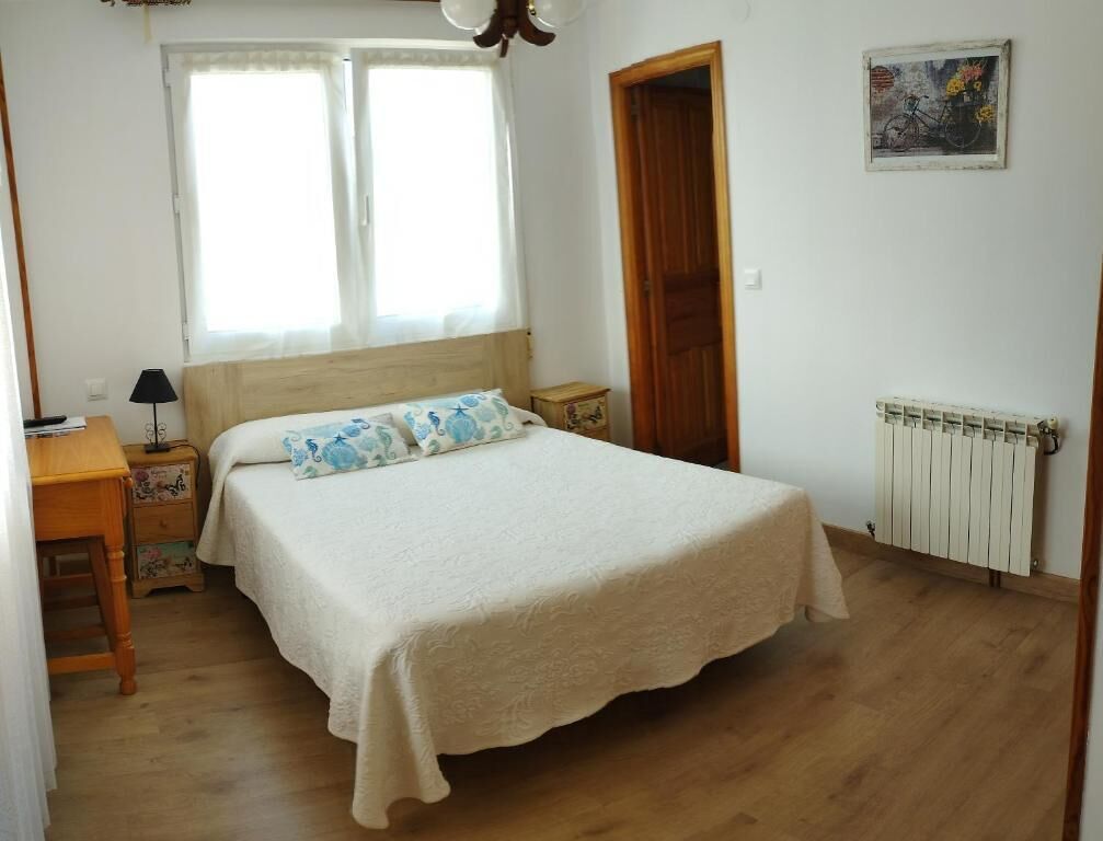 Una camera da letto con un letto grande, un comodino, una lampada, un pavimento in legno, una finestra e un termosifone.