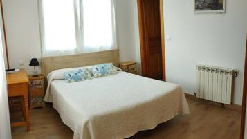 Una camera da letto con un letto grande, un comodino, una lampada, un pavimento in legno, una finestra e un termosifone.