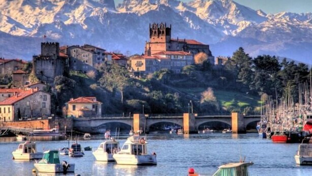 A coastal town with a historic castle, a bridge, and boats in the harbor. - Alto Santiago (San Vicente de la Barquera)