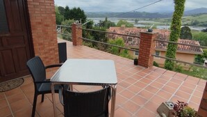 A balcony with a table and chairs, a view of a river and distant landscape, and a brick wall. - Alto Santiago (San Vicente de la Barquera)