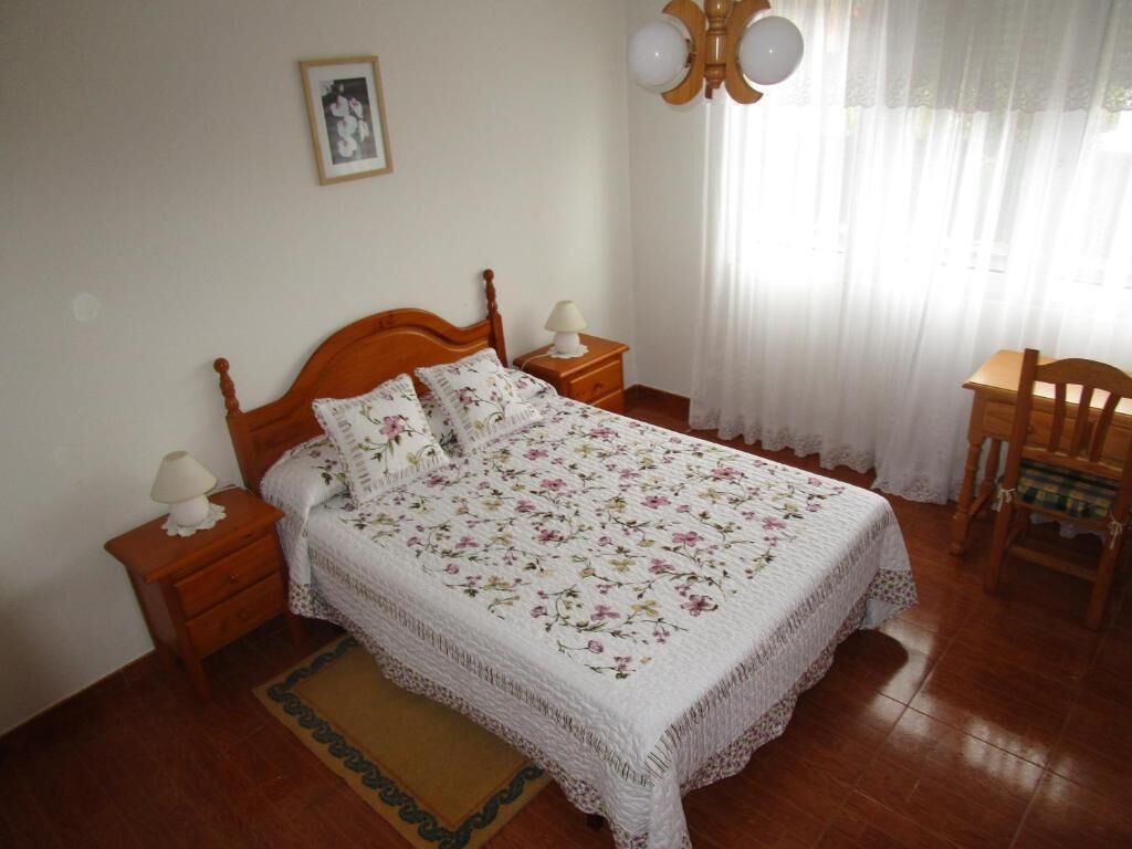 Een netjes ingerichte slaapkamer met een bed, twee nachtkastjes, een stoel en een raam met gordijnen.