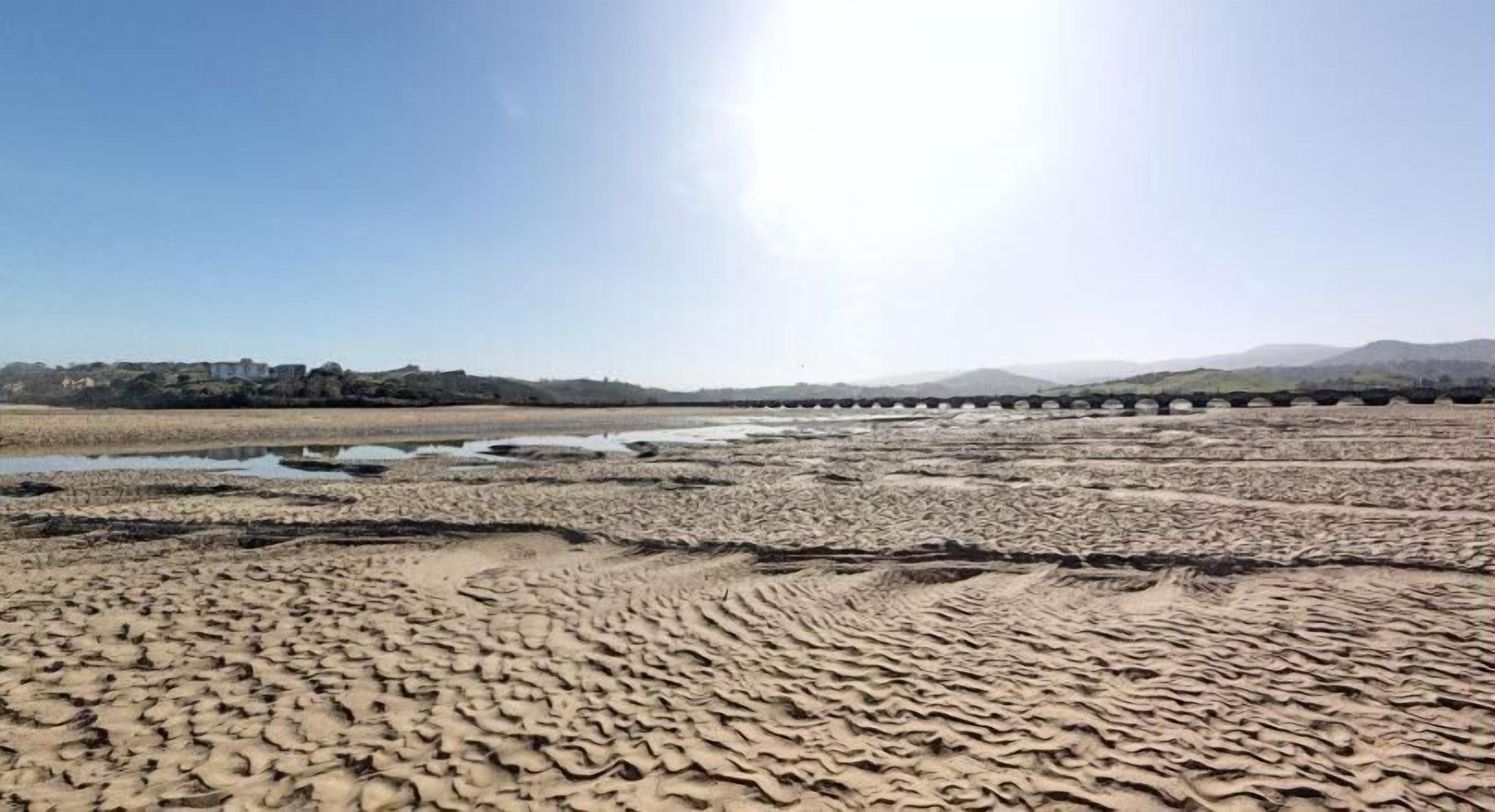 A dry, textured landscape with a river and distant hills.