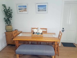 Enjoy meals in this cozy dining area with a wooden table and bench, set with a tray, framed pictures, and a potted plant.