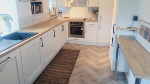 Una cocina moderna con armarios blancos, encimera de madera, horno empotrado y suelo con patrón de espiga.