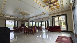 Una habitación amplia con suelo de mármol, un comedor con muebles de madera, un sofá rojo y grandes ventanas que ofrecen vistas al exterior.