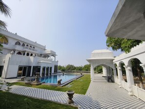 A courtyard with a swimming pool, a checkered tiled walkway, and a white building with arches and columns.