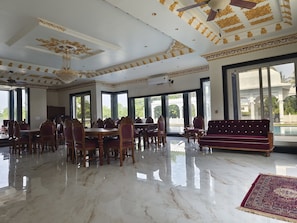 A spacious dining area with a marble floor, large windows, and a red sofa.