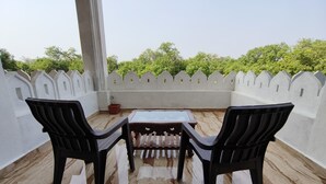 Una terraza con una mesa y dos sillas, una pared blanca con detalles decorativos y vistas a zonas verdes.