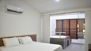 Een slaapkamer met een bed, een airconditioner, een badkamer met een wastafel en uitzicht op buiten.