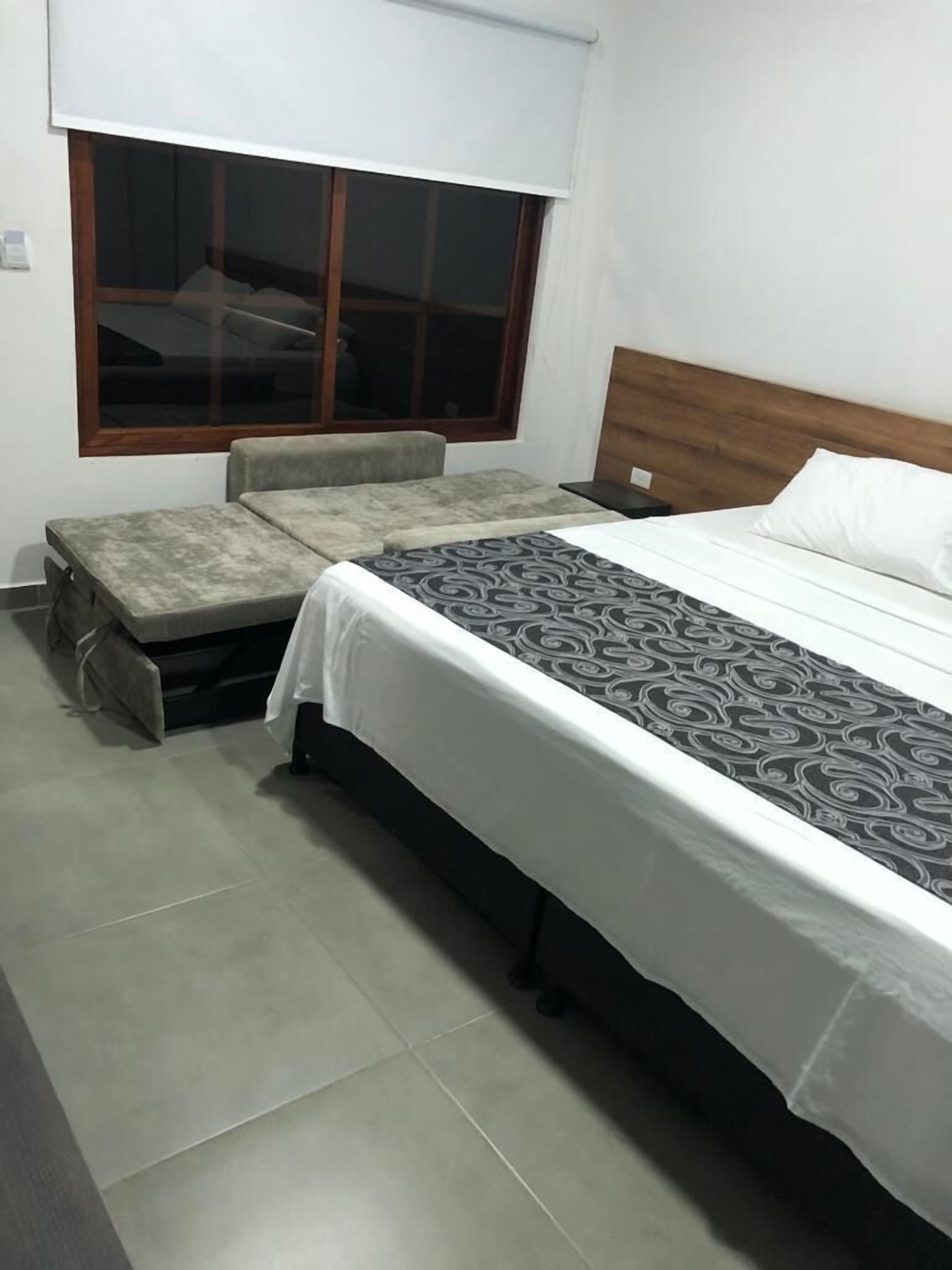 Une chambre à coucher avec un lit, un banc, une fenêtre et une table de chevet.