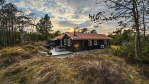 Une cabane avec un toit rouge, entourée d’arbres et d’un terrain herbeux.