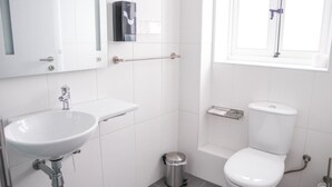 A modern bathroom with a white sink, toilet, and a small trash bin. - AM Hostel (Sliema)