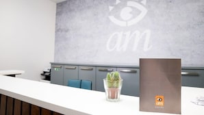 A reception area with a modern design, featuring a grey wall with a logo and the word "am" in white. There's a small cactus plant on the counter, and a brown folder with the "am" logo. - AM Hostel (Sliema)
