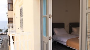 A hotel room with a bed, a window with blue curtains, and a balcony with a railing. - AM Hostel (Sliema)