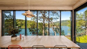 Ein Essbereich mit Holztisch und Metallstühlen, große Fenster mit Blick auf einen See und Bäume.