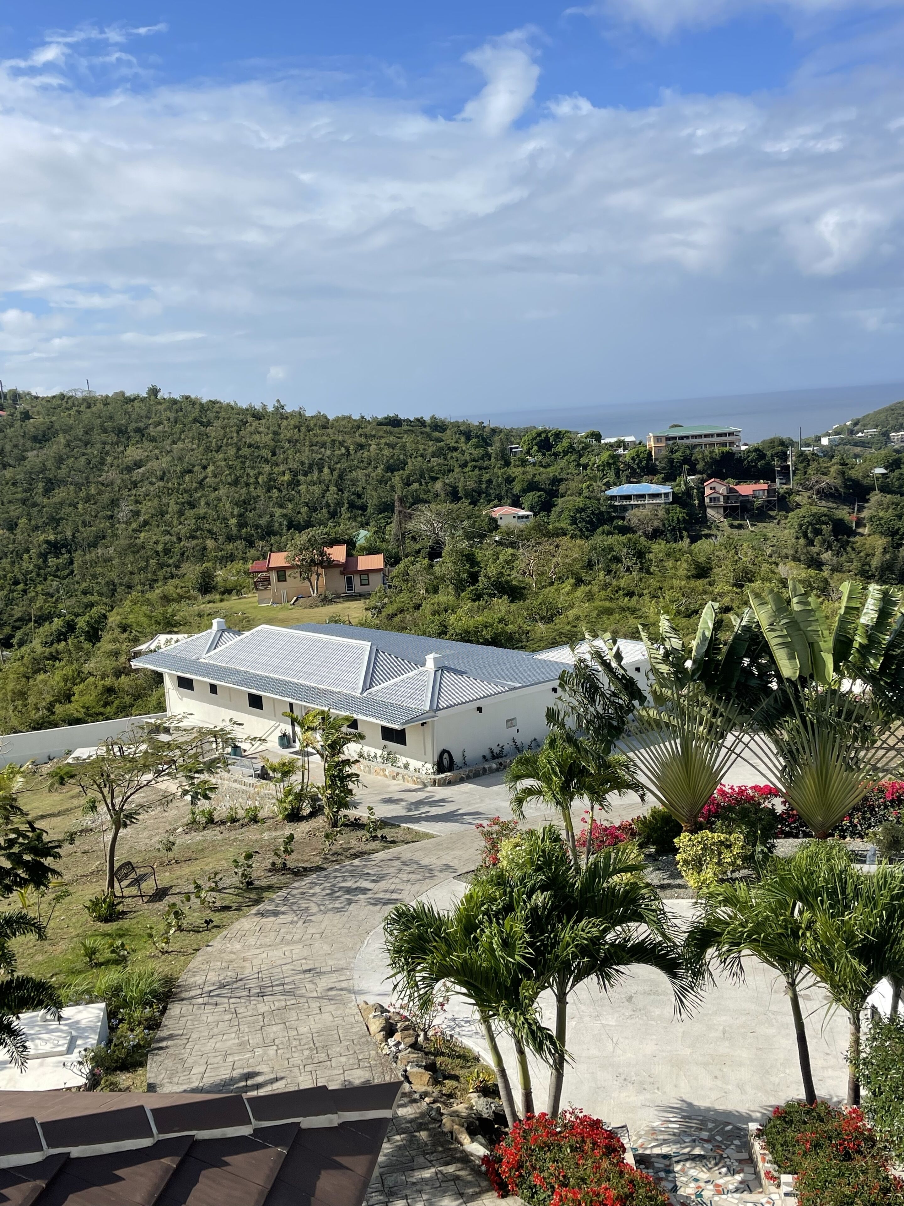 A modern building with a flat roof, surrounded by lush greenery and a clear view of the sea.