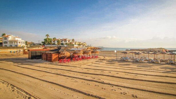 A beach with red chairs and umbrellas, a small hut, and buildings in the background. - Gorgeous apartment in Torrevieja (Torrevieja)