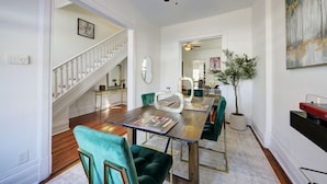 Een eetgedeelte met een houten tafel, groene bekleden stoelen, een plafondventilator en een potplant.