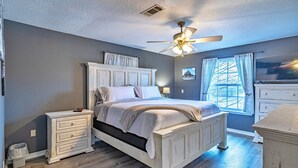 Een slaapkamer met een bed, nachtkastjes, een dressoir, een plafondventilator en een raam met gordijnen.