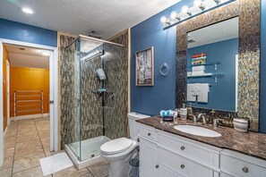 Ein Badezimmer mit Duschkabine aus Glas, einer weißen Toilette, einem Waschbecken mit Marmorplatte und einem großen Spiegel mit Mosaikfliesen-Verkleidung.