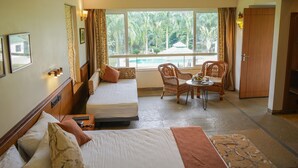 A hotel room with two beds, a dining area with wicker chairs, a view of a pool, and a wardrobe. - Village Machaan Resort (Kurai)