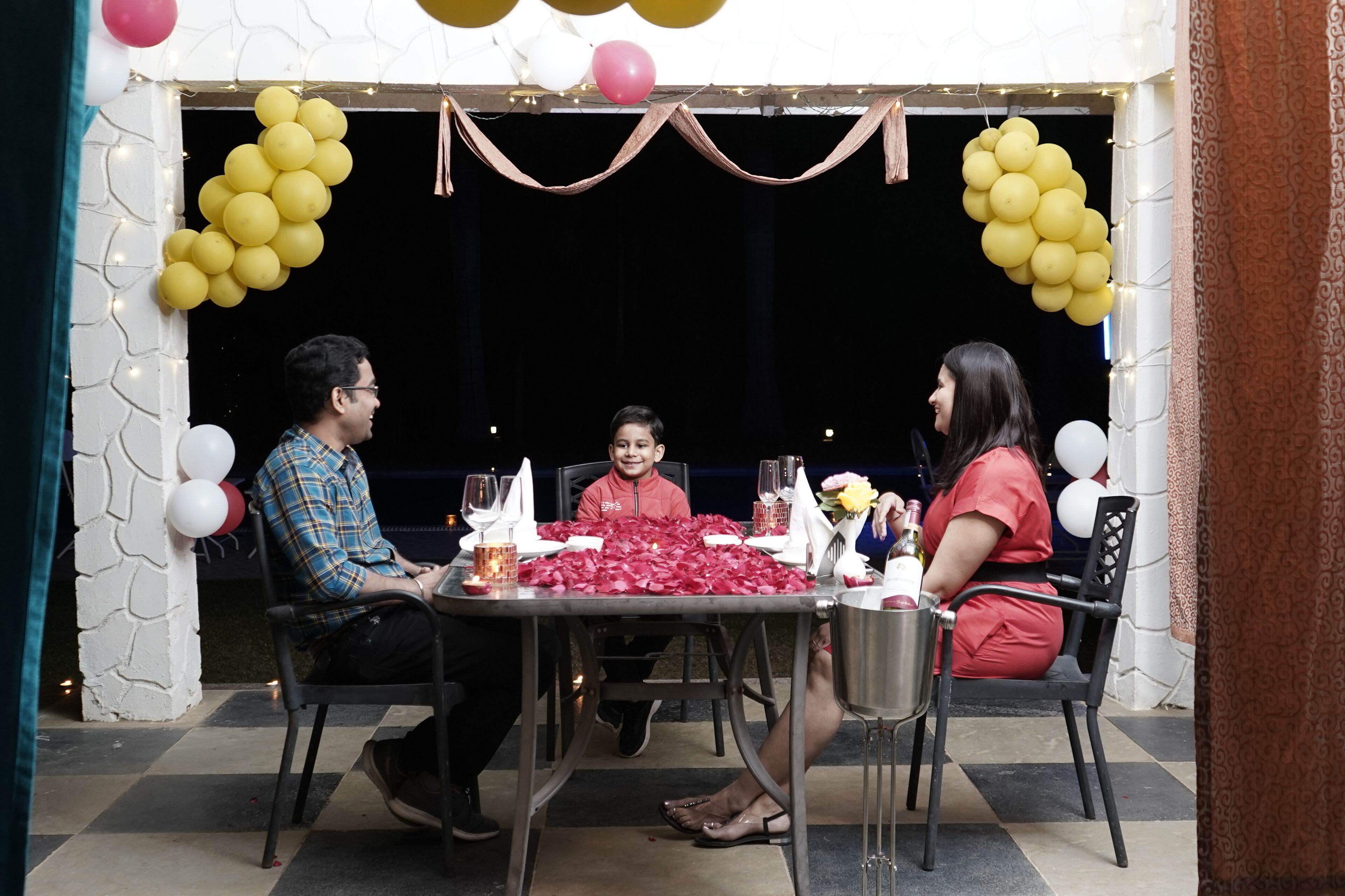Comedor con mesa preparada para tres, decorado con globos y pétalos de rosa.