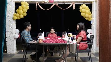 Comedor con mesa preparada para tres, decorado con globos y pétalos de rosa.