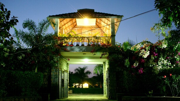 An open archway leading to a covered area with a light source above, surrounded by greenery and flowering plants. - Village Machaan Resort (Kurai)