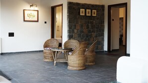 A spacious lobby with wicker chairs, a stone wall, and framed artwork. - Village Machaan Resort (Kurai)