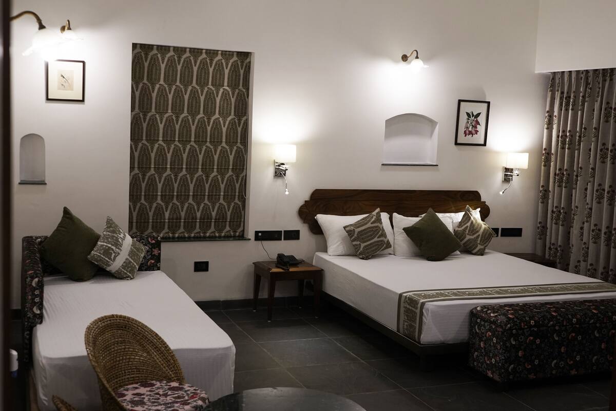 A hotel room with two beds, a small table, a chair, and a large patterned wall.