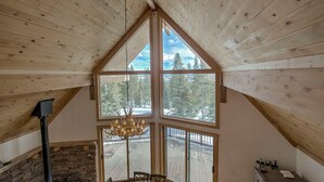 Ein Raum mit hohen Decken, großen Fenstern, einem Kamin aus Stein und einer Kristallleuchter.
