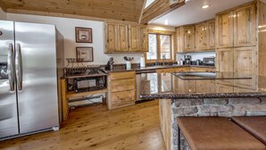 Eine geräumige Küche mit Holzschränken, einem Edelstahlkühlschrank, einer Granitarbeitsplatte und einer Wand mit Natursteinverkleidung.
