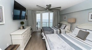 Une chambre d’hôtel équipée d’un lit, d’une table de chevet, d’une lampe, d’une télévision, d ’un ventilateur de plafond et offrant une vue sur la mer.