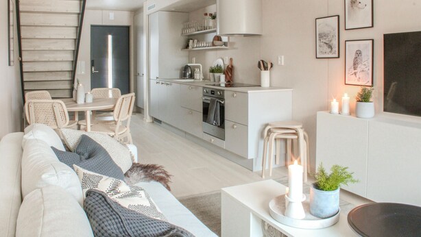 Un salon moderne comprenant un canapé, une table basse et un coin repas avec des chaises. Il y a également une cuisine équipée de placards et d'une cuisinière.