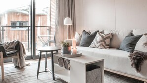 Un salon moderne avec un canapé, une petite table d’appoint avec une lampe, un fauteuil et une vue sur une terrasse en bois à l’extérieur.